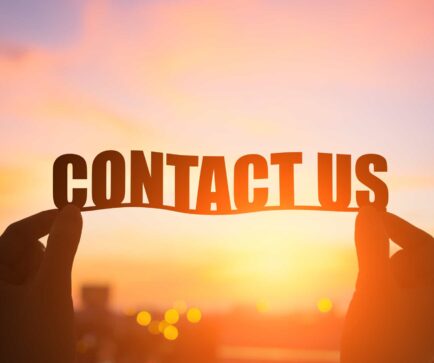 A person holding up a contact us sign in front of a sunset.